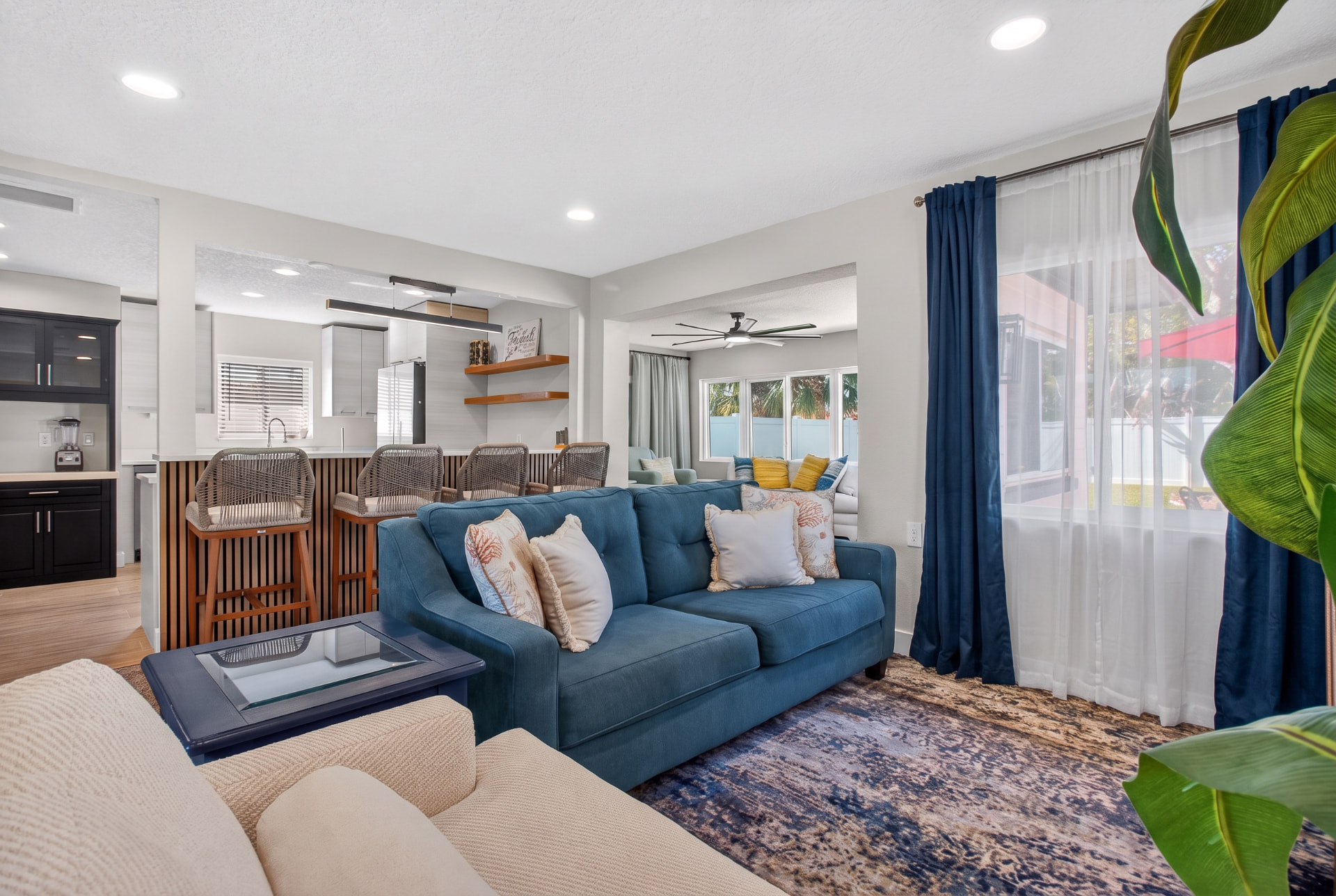 Bright living room with navy curtains, a blue sofa, and a view toward the kitchen and sunroom