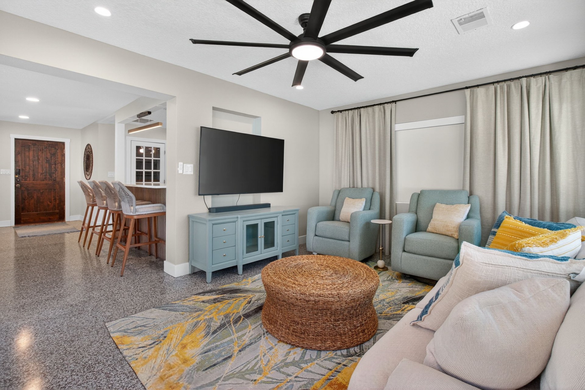 Living room with wide ceiling fan, glider chairs, and mounted television
